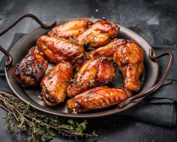 Saftige Hähnchenflügel in einer glänzenden Marinade, garniert mit frischem Thymian, serviert auf einer dunklen Platte.