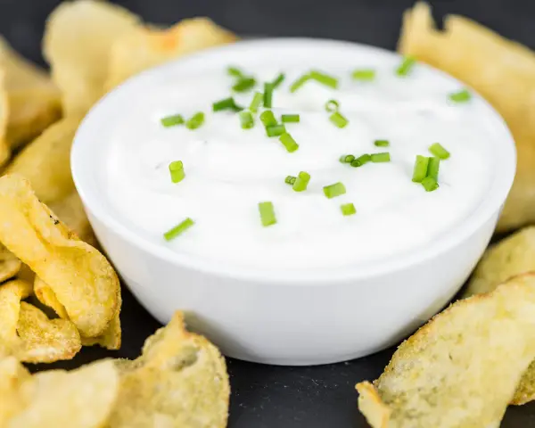 Schüssel mit cremiger Sour Cream, garniert mit Schnittlauch, umgeben von knusprigen Kartoffelchips.
