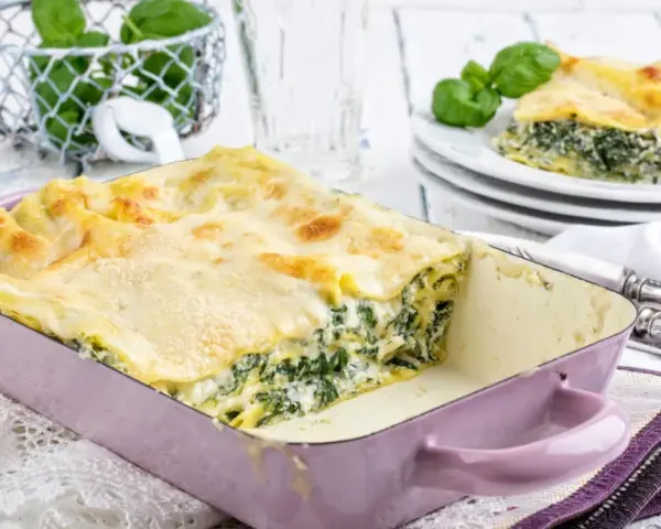 Herzhaftes Spinat-Lasagne-Rezept in einer lila Auflaufform, mit frischem Basilikum garniert.