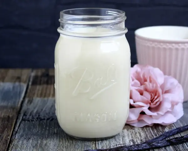 Selbstgemachter Kaffee-Sirup in einem Glas, mit Vanilleschoten und einer rosa Blume. Perfekt zum Kaffee creamer selber machen.