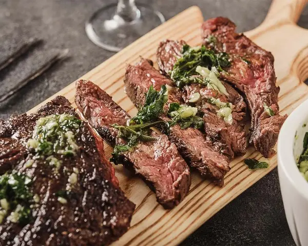 Saftiges, in Scheiben geschnittenes Flank Steak mit Kräutern und einer grünen Sauce auf einem Holzbrett serviert.