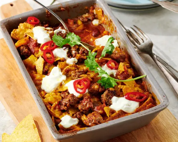 Herzhafter Shepherd's Pie mit Hackfleisch, Tortilla-Chips, Chili-Ringen und Klecksen saurer Sahne, garniert mit Koriander.