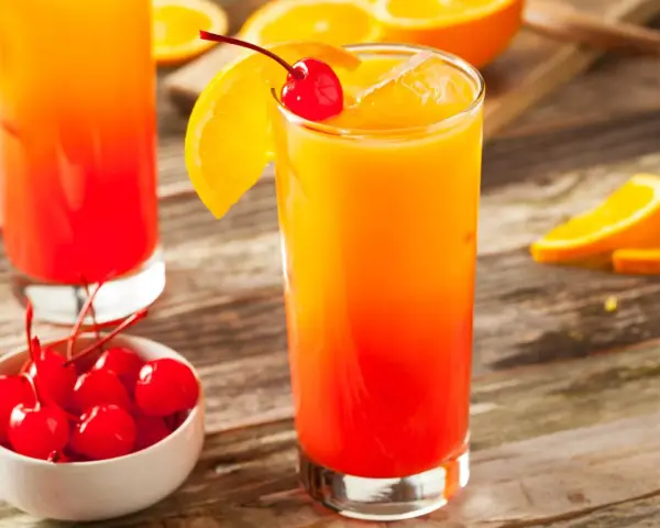 Ein erfrischender Tequila Sunrise mit Orangenscheibe und Kirsche, daneben eine Schale mit Kirschen.