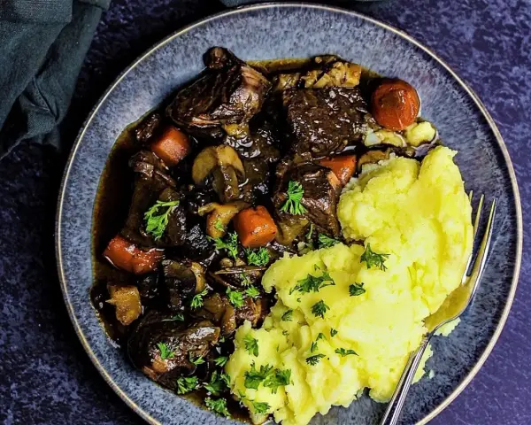 Herzhaftes Boeuf Bourguignon mit zartem Rindfleisch, Karotten und Pilzen, serviert mit cremigem Kartoffelpüree und Petersilie.