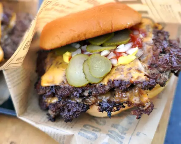 Saftiger Smash Burger mit geschmolzenem Käse, Gurken, Zwiebeln und Ketchup auf einem Brötchen, eingewickelt in Papier.