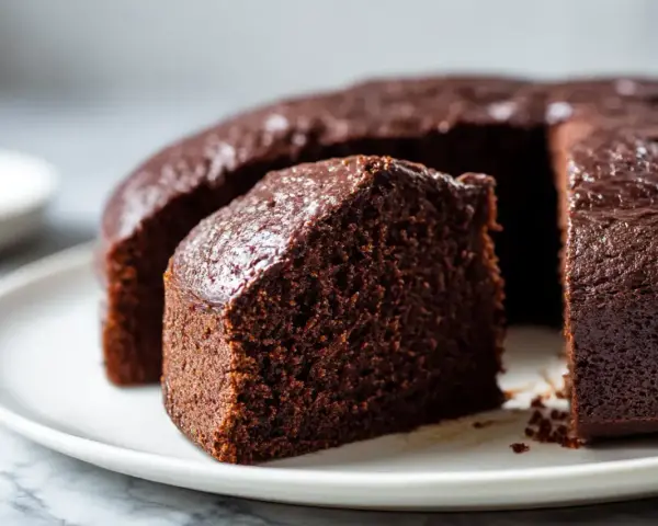 Saftiger Schokoladenkuchen, frisch aus dem Airfryer, auf einer weißen Platte. Ein Stück ist bereits angeschnitten.