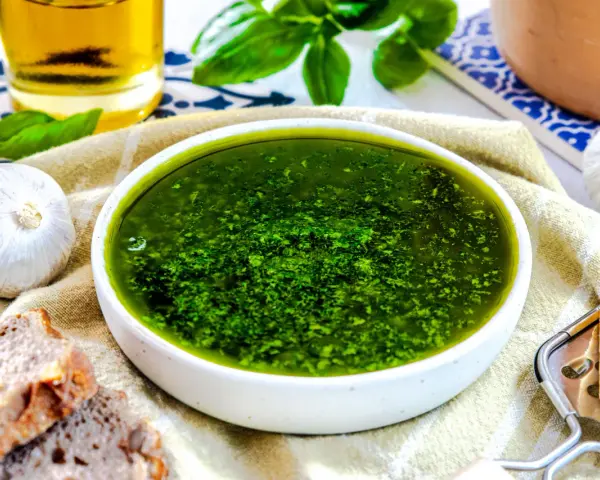 Frisches, grünes Pesto ohne Pinienkerne in einer Schüssel, daneben Knoblauch, Brot und Parmesan.