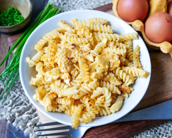 Fusilli-Nudeln mit Rührei, gewürzt mit Pfeffer. Daneben liegen frische Eier und Schnittlauch. Ein einfaches, aber leckeres Gericht: Nudeln mit Ei.