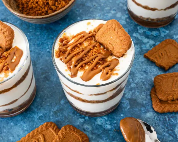 Schichtdessert im Glas: cremiges Lotus Cheesecake mit Keksbröseln und Karamellsoße, garniert mit einem Lotus Keks.