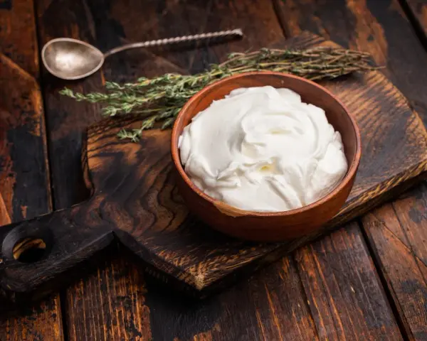 Cremiger, selbstgemachter Haferjoghurt in einer Holzschale, bereit zum Genießen. Ein Löffel und Kräuter liegen daneben.