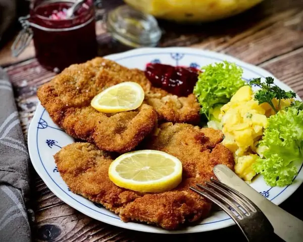Ein köstlicher **Garnitur Wiener Schnitzel** mit Kartoffelsalat, Preiselbeeren und Zitrone auf einem Teller.