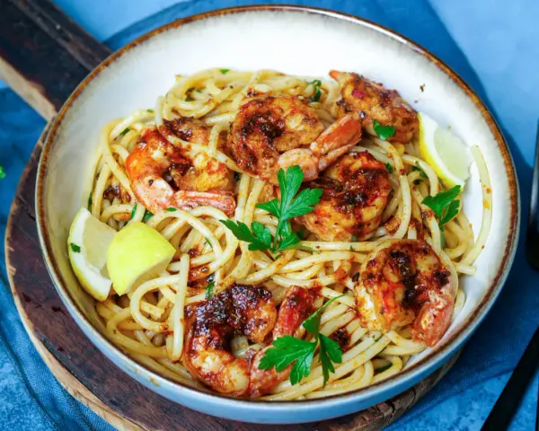 Ein Teller mit köstlichen Spaghetti mit Garnelen, garniert mit frischer Petersilie und Zitronenspalten.