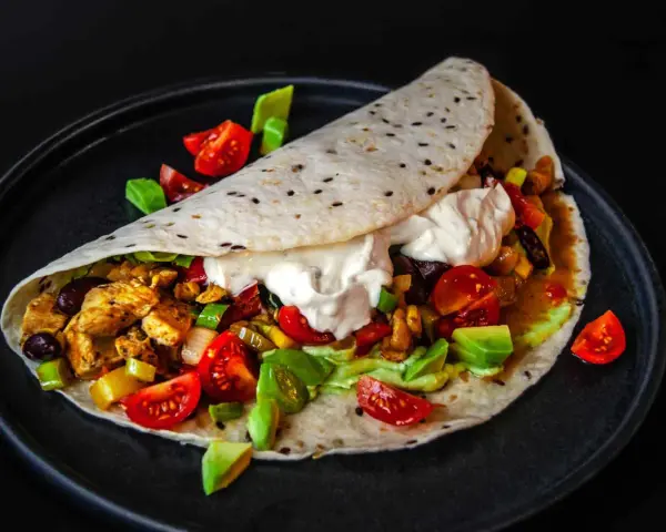 Saftige Fajitas de pollo mit Hähnchen, Gemüse, Avocado und einem Klecks Sauerrahm auf einem Tortilla-Wrap.