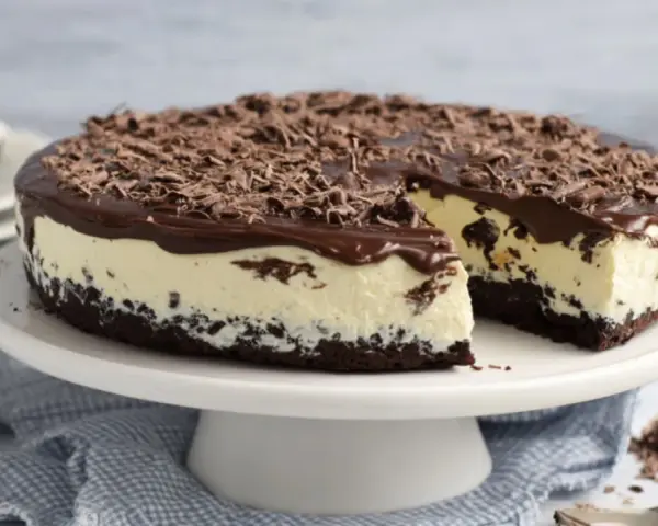 Eine köstliche Bananensplit Torte ohne Backen, mit Schokoladenüberzug und Schokostreuseln. Ein Stück ist bereits angeschnitten.
