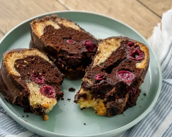 Drei saftige Stücke Marmorkuchen mit Kirschen und Schokoladenglasur auf einem Teller.