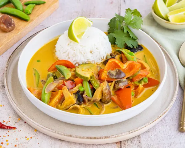 Ein bunter Thai Curry ohne Kokosmilch mit Reis, Paprika, Zucchini und Pilzen, garniert mit Limette und Koriander.