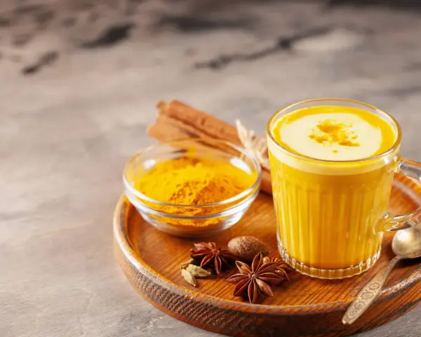 Ein Glas goldene Milch mit Kurkumapulver, Zimtstangen und Sternanis. Perfekt für ein wärmendes goldene milch rezept.