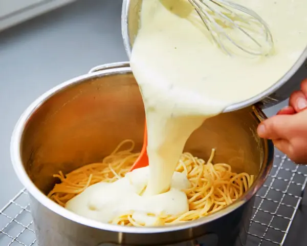 Cremige Käsesauce wird über Spaghetti gegossen. Ein einfaches Käsesauce Rezept für ein köstliches Gericht.