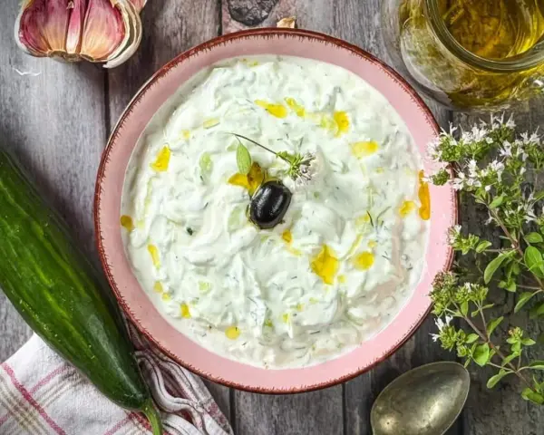 Frischer Tzatziki selbst machen: Cremiger Joghurt mit Gurke, Knoblauch, Dill und Olivenöl. Dazu eine Olive und Kräuter.