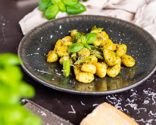 Gnocchi mit Spargel, garniert mit frischem Basilikum und Parmesan. Ein köstliches Gericht, das den Frühling auf den Teller bringt.