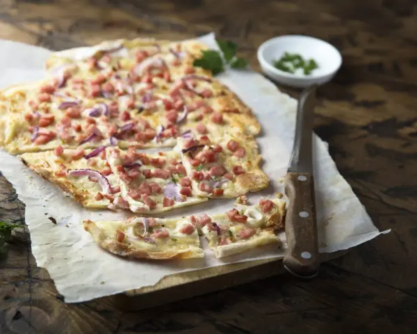 Flammkuchen mit Speck und Zwiebeln, eine klassische Idee für Flammkuchen Belag. Frisch und knusprig auf Holz serviert.