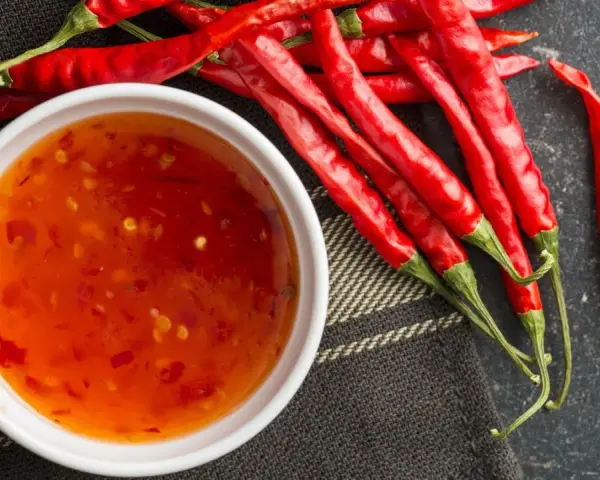 Frische rote Chilis neben einer Schüssel mit selbstgemachter Chili-Sauce. Perfekt zum Chili Sauce selber machen!
