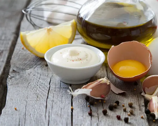Cremige Mayonnaise mit gekochtem Eigelb und Joghurt, garniert mit Pfeffer, neben Zitrone, Knoblauch und Olivenöl.