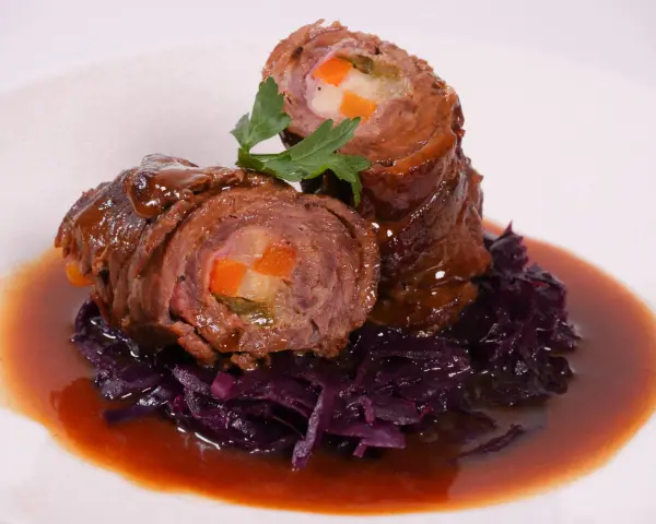 Zwei Rouladen mit Gemüsefüllung, serviert mit Rotkohl und Bratensoße. Köstliche Rouladen im Backofen zubereitet.