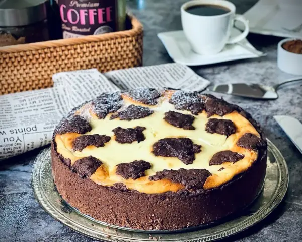 Ein köstlicher russischer Zupfkuchen mit Schokoladenboden und cremiger Füllung, bestäubt mit Puderzucker. Daneben eine Tasse Kaffee.