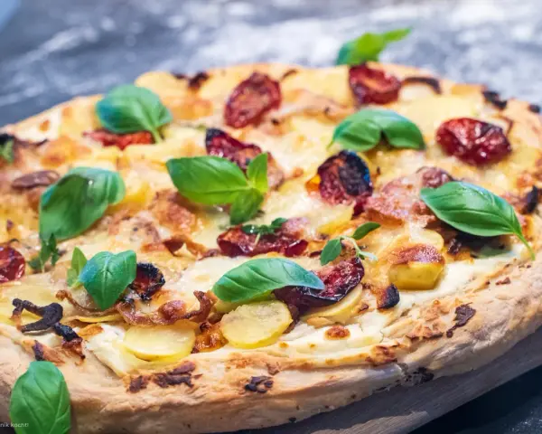 Eine köstliche Pizza Bianca mit Kartoffelscheiben, getrockneten Tomaten und frischem Basilikum.