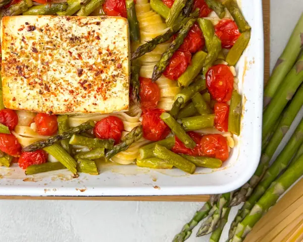 Spargel, Kirschtomaten und Pasta mit einem Block Feta, gewürzt mit Kräutern, in einer Auflaufform.