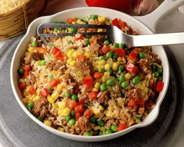 Reis mit Hackfleisch, Erbsen, Mais und Paprika in einer Schüssel, serviert mit einer Gabel.