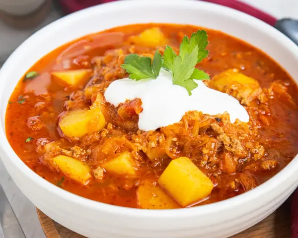 Herzhafte Mitternachtssuppe mit Hackfleisch und Sauerkraut, garniert mit einem Klecks Sauerrahm und Petersilie.