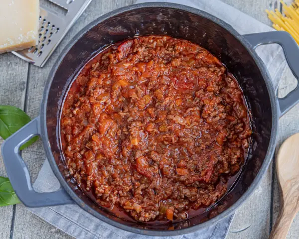 Herzhaftes Bolognese-Rezept original in einem Topf, mit frischem Basilikum, Parmesan und Spaghetti daneben.