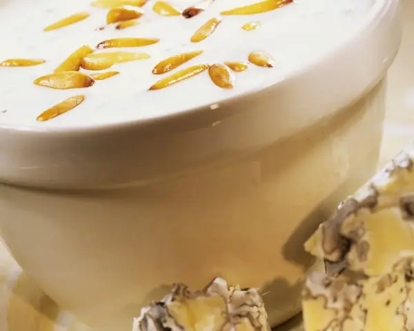 Cremige Gorgonzola-Sauce mit gerösteten Pinienkernen in einer Schüssel, daneben ein Stück Gorgonzola.