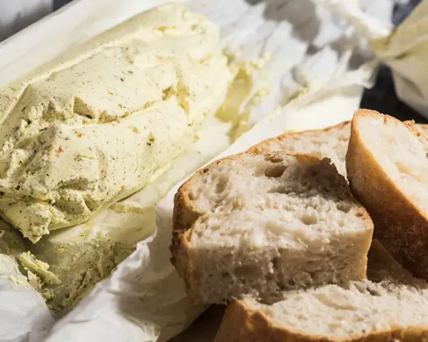 Ein Laib Kräuterbutter, wie Cafe de Paris Butter, liegt neben frisch geschnittenem Baguette.