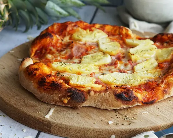 Eine köstliche Pizza Hawaii mit saftigen Ananasstücken und Schinken auf knusprigem Teig, garniert mit Kräutern.
