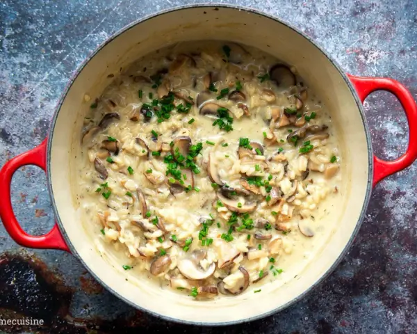 Cremiges Pilzrisotto in rotem Topf, garniert mit Schnittlauch.