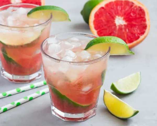 Erfrischender Aperol Paloma mit Grapefruit und Limette, serviert mit Eis und grünen Trinkhalmen.