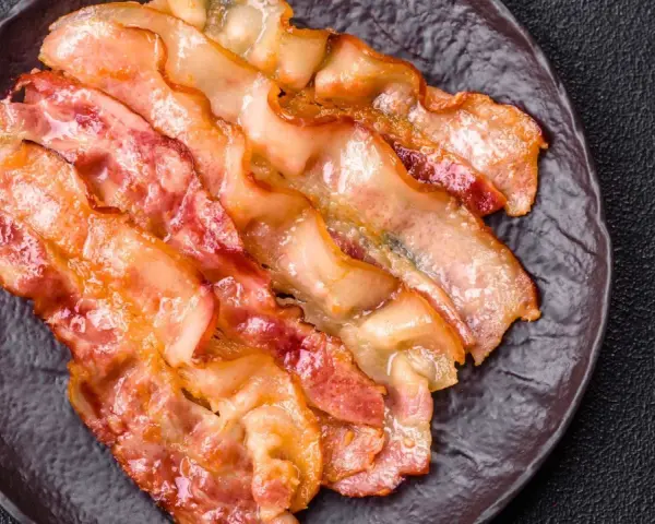 Knusprig gebratener Bacon im Ofen, auf einem dunklen Teller angerichtet.