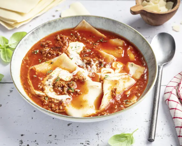 Herzhafte Lasagne Suppe in einer Schüssel, mit Hackfleischsauce, Nudelplatten und einem Klecks Sahne. Frisch garniert mit Basilikum.