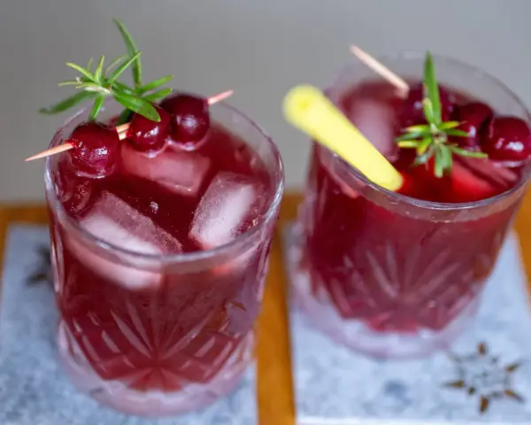 Zwei erfrischende, rote Mocktails mit Kirschen und Rosmarin, perfekt für einen entspannten Abend.