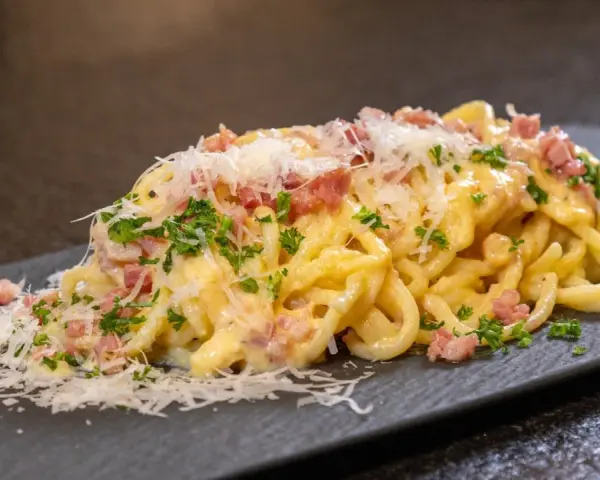 Ein Teller cremiger Spaghetti Carbonara, garniert mit Speckwürfeln, Petersilie und frisch geriebenem Parmesan.