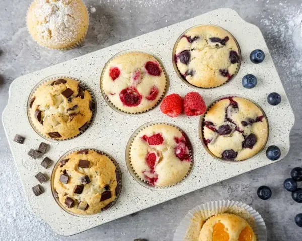 Leckeres Muffins Rezept: Schoko-, Himbeer- und Blaubeermuffins in einer Form, daneben frische Beeren und Schokostückchen.