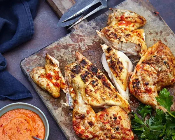 Saftiges Peri Peri Chicken, gegrillt und mit einer würzigen Sauce serviert, liegt auf einem Holzbrett.