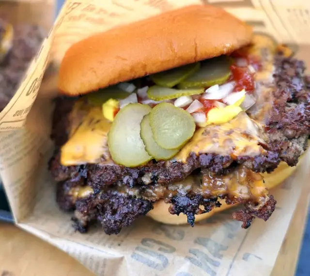 Saftiger Smash Burger mit geschmolzenem Käse, Gurken, Zwiebeln und Ketchup auf einem Brötchen, eingewickelt in Papier.