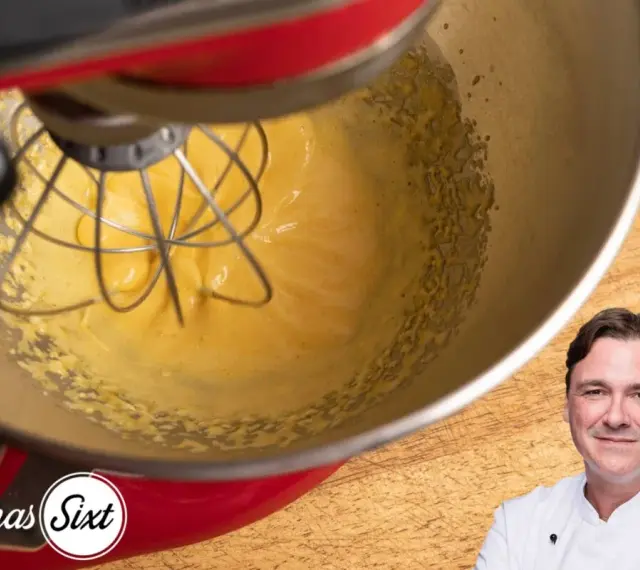 Küchenmaschine mixt eine cremige, gelbe Masse, die an Sauce Hollandaise erinnert. Ein Koch lächelt im Vordergrund.