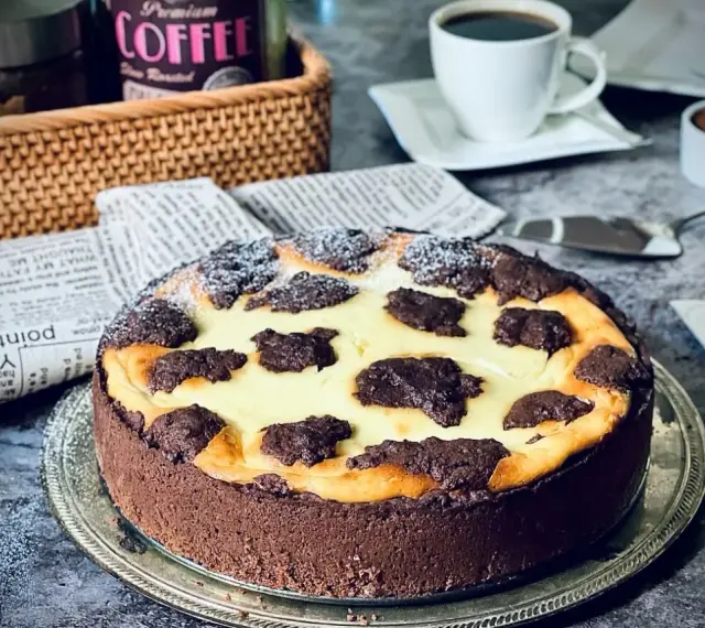 Ein köstlicher russischer Zupfkuchen mit Schokoladenboden und cremiger Füllung, bestäubt mit Puderzucker. Daneben eine Tasse Kaffee.