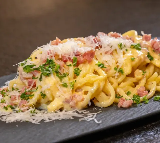 Ein Teller cremiger Spaghetti Carbonara, garniert mit Speckwürfeln, Petersilie und frisch geriebenem Parmesan.