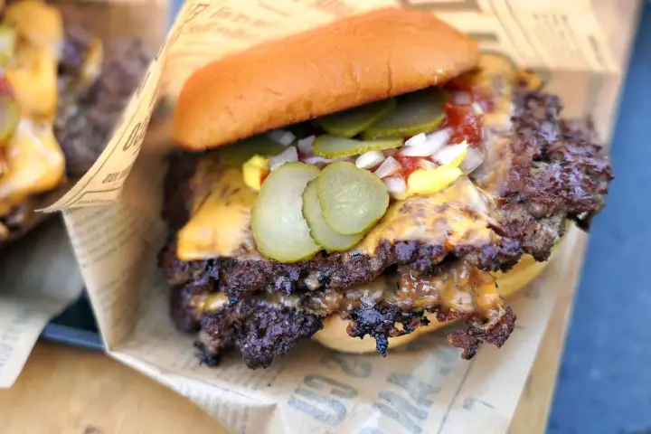 Saftiger Smash Burger mit geschmolzenem Käse, Gurken, Zwiebeln und Ketchup auf einem Brötchen, eingewickelt in Papier.